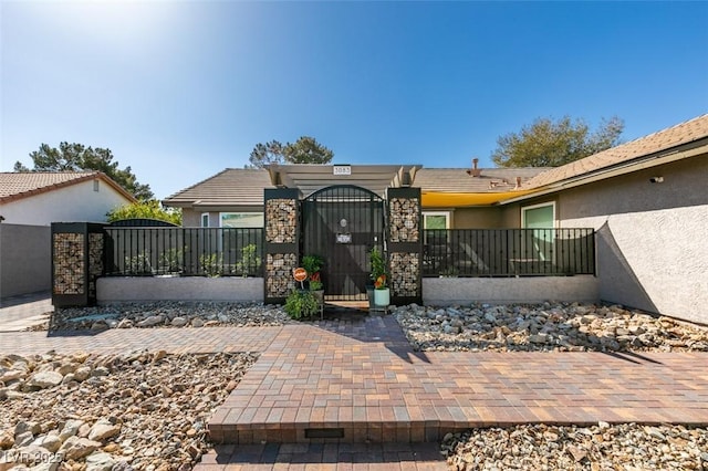 view of front of house with stucco siding, stone siding, a fenced front yard, and a gate