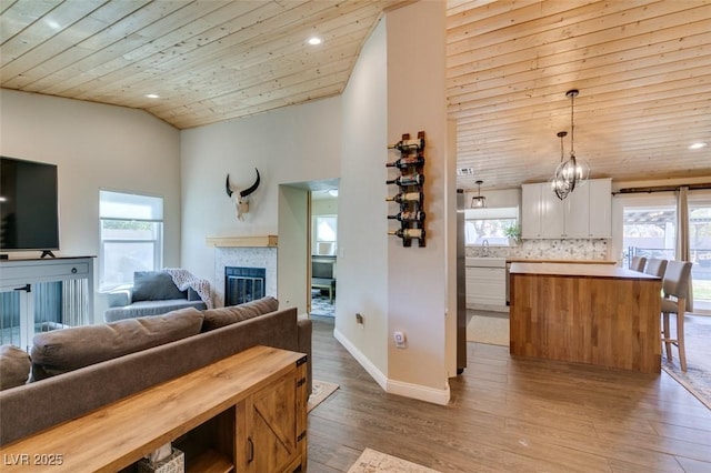 living area featuring a wealth of natural light, a glass covered fireplace, wood ceiling, and light wood-type flooring