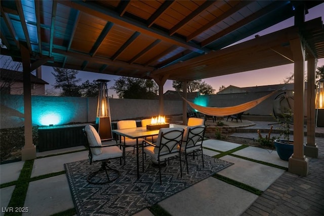 patio terrace at dusk featuring outdoor dining area, fence, and a fire pit