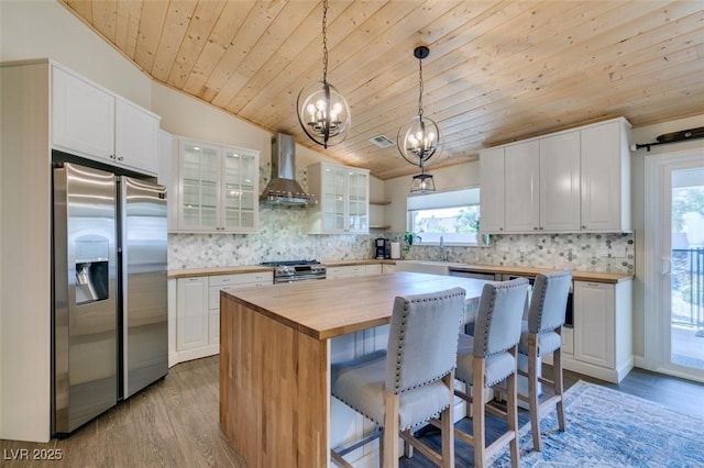 kitchen with wooden counters, a kitchen island, decorative backsplash, stainless steel appliances, and wall chimney exhaust hood