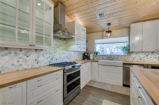 kitchen with butcher block countertops, appliances with stainless steel finishes, extractor fan, and a sink