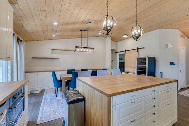 kitchen featuring dark wood finished floors, butcher block countertops, lofted ceiling, a barn door, and white cabinetry