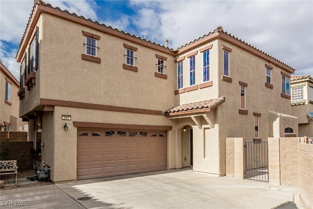 mediterranean / spanish home with fence, a tiled roof, concrete driveway, stucco siding, and an attached garage