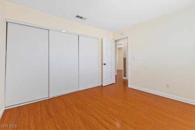 unfurnished bedroom with a closet, visible vents, baseboards, and wood finished floors