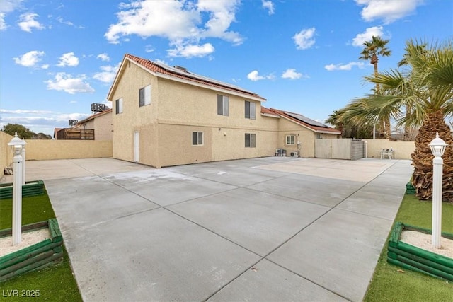 rear view of property featuring a gate, stucco siding, solar panels, and fence