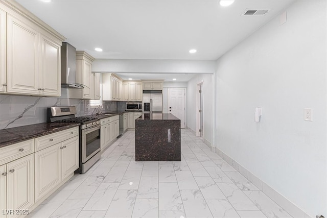 kitchen featuring visible vents, stainless steel appliances, cream cabinets, wall chimney range hood, and marble finish floor