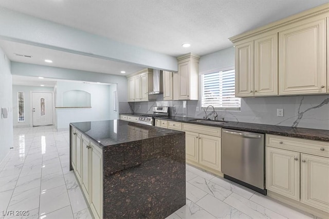 kitchen featuring marble finish floor, a sink, cream cabinets, appliances with stainless steel finishes, and wall chimney exhaust hood