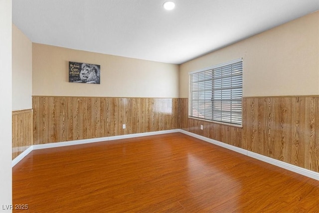 empty room with wood finished floors, wood walls, and wainscoting