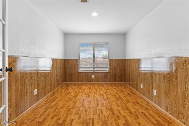 unfurnished room with wooden walls, wood finished floors, and wainscoting