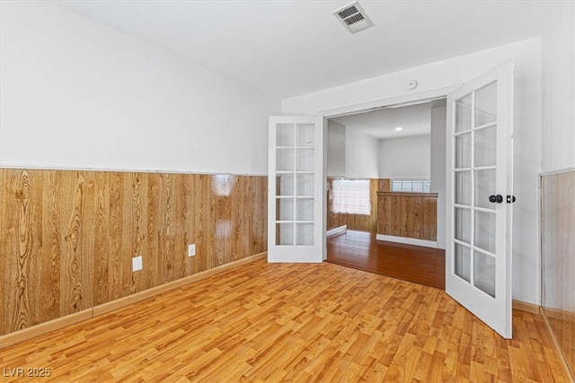 unfurnished room featuring wooden walls, wood finished floors, a wainscoted wall, visible vents, and french doors