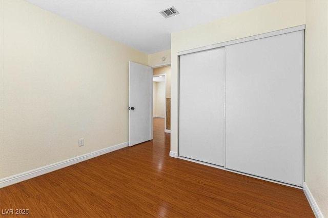 unfurnished bedroom featuring visible vents, baseboards, a closet, and wood finished floors