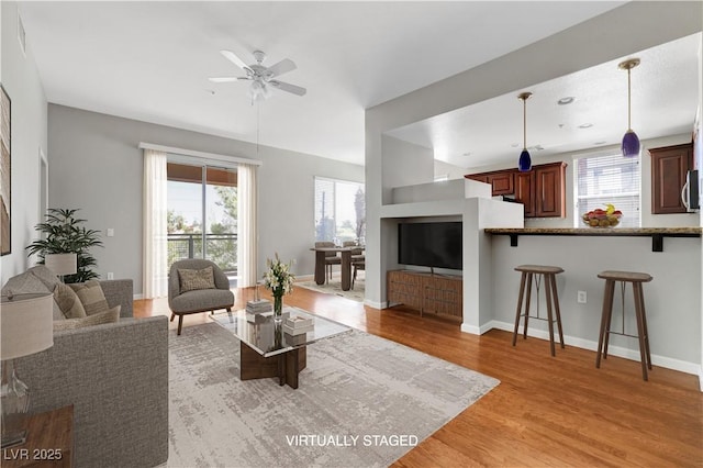 living room featuring a ceiling fan, a healthy amount of sunlight, baseboards, and light wood finished floors