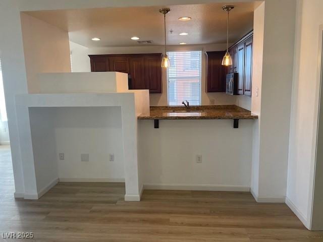 kitchen featuring decorative light fixtures, stainless steel microwave, light wood-style flooring, and a breakfast bar area