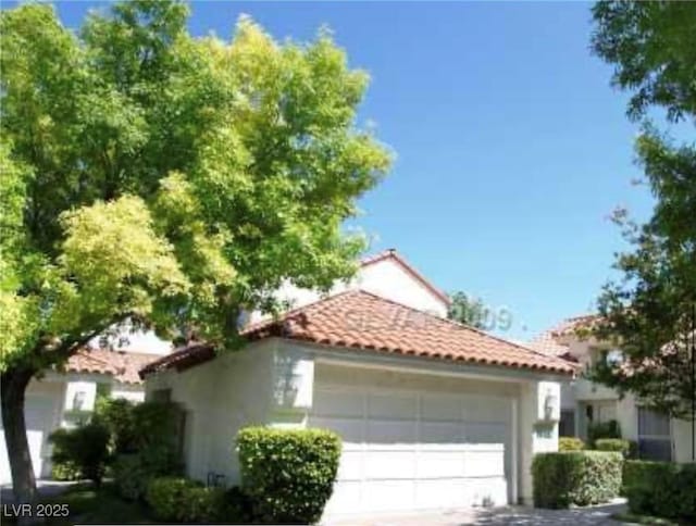 view of side of home with stucco siding, a tiled roof, driveway, and a garage