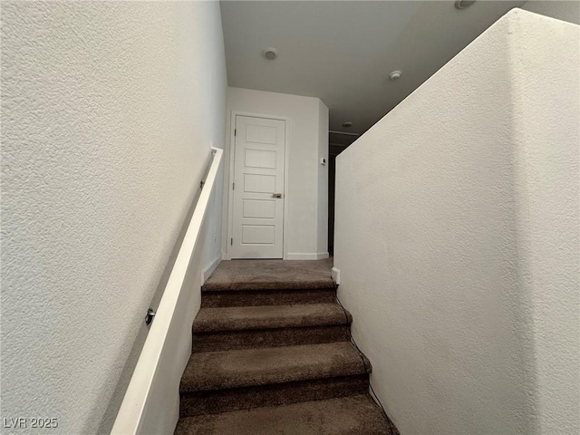 stairs featuring carpet, a textured wall, and baseboards