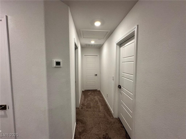 corridor with dark colored carpet, visible vents, baseboards, and attic access