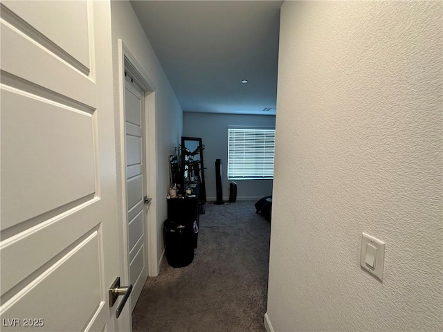 corridor with a textured wall, dark colored carpet, and baseboards