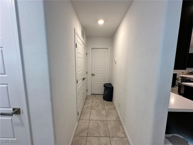 hallway with light tile patterned floors, visible vents, and baseboards