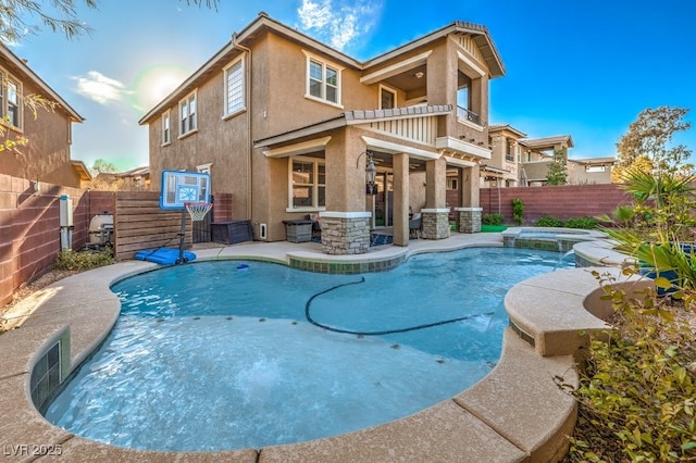 rear view of property with stucco siding, a pool with connected hot tub, a fenced backyard, and a patio area