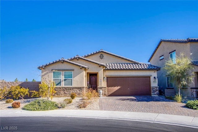 mediterranean / spanish-style home with a tile roof, stucco siding, decorative driveway, a garage, and stone siding