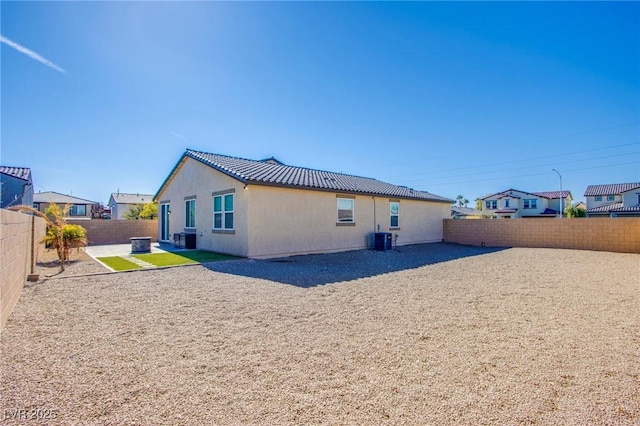 back of property with a fenced backyard, stucco siding, a tiled roof, and central AC