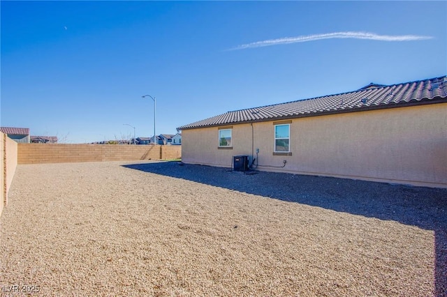 rear view of property with a tiled roof, a fenced backyard, central AC, and stucco siding