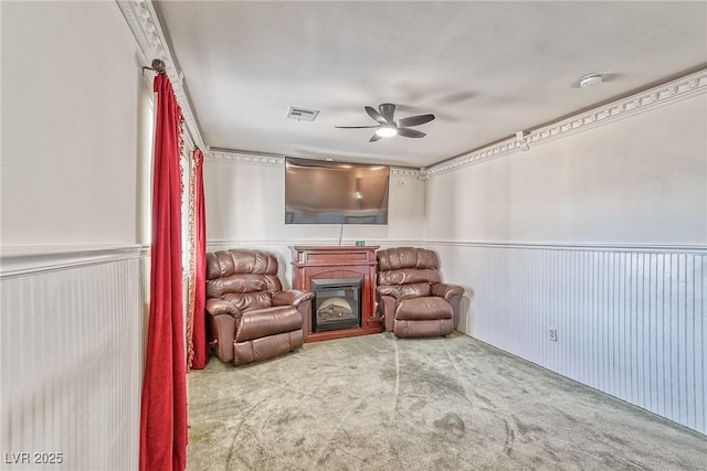 living area with visible vents, carpet, a wainscoted wall, a fireplace, and a ceiling fan