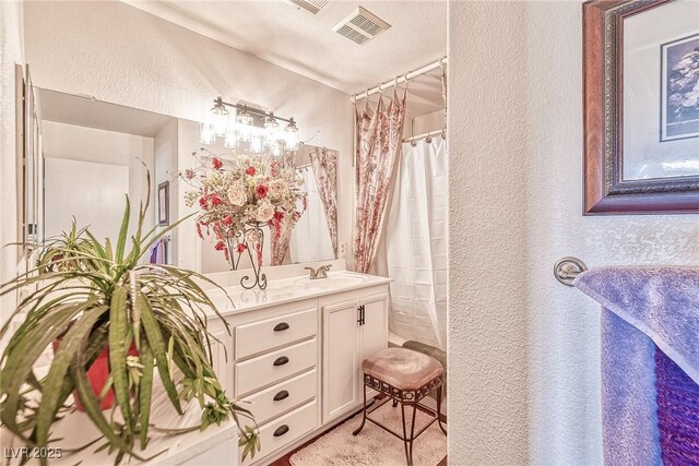 full bath with vanity, a shower with shower curtain, a textured wall, and visible vents