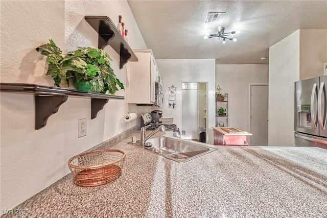 kitchen with appliances with stainless steel finishes, a textured wall, a textured ceiling, white cabinetry, and a sink