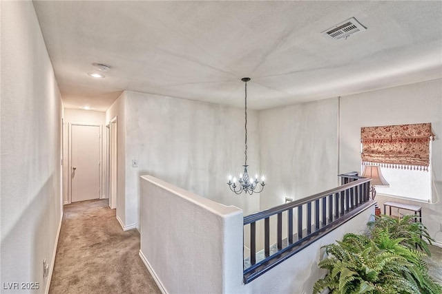 hall featuring visible vents, an upstairs landing, carpet floors, an inviting chandelier, and baseboards