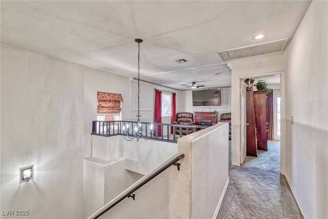 hall featuring an inviting chandelier, an upstairs landing, visible vents, and carpet floors