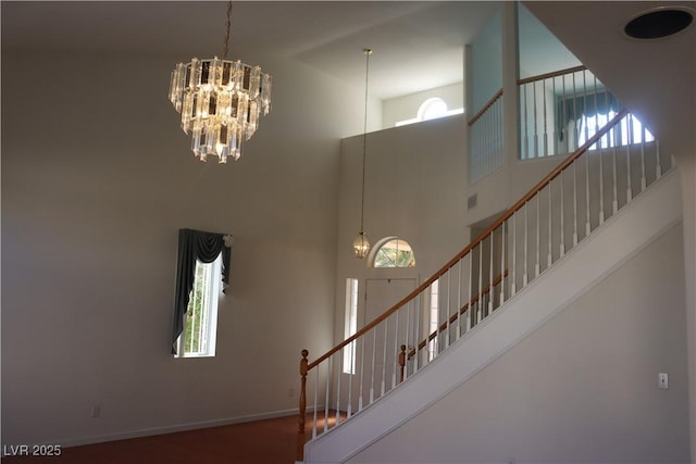 stairs featuring a healthy amount of sunlight, a towering ceiling, and an inviting chandelier