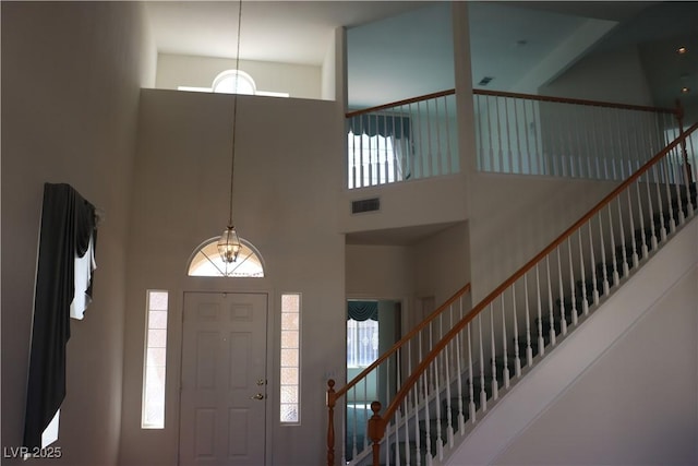 entryway with visible vents, a healthy amount of sunlight, a towering ceiling, and stairs