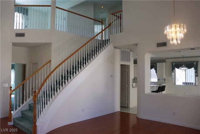 stairs with wood finished floors, visible vents, a towering ceiling, and baseboards