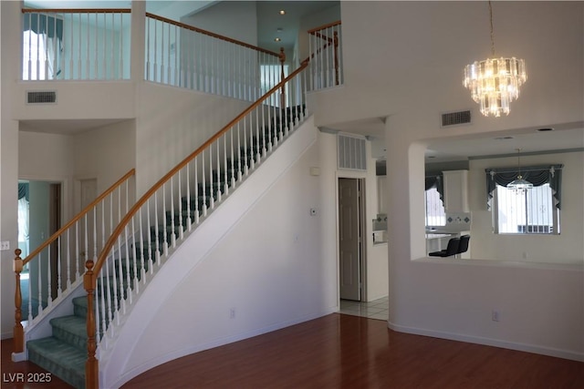 staircase featuring a high ceiling, wood finished floors, visible vents, and baseboards