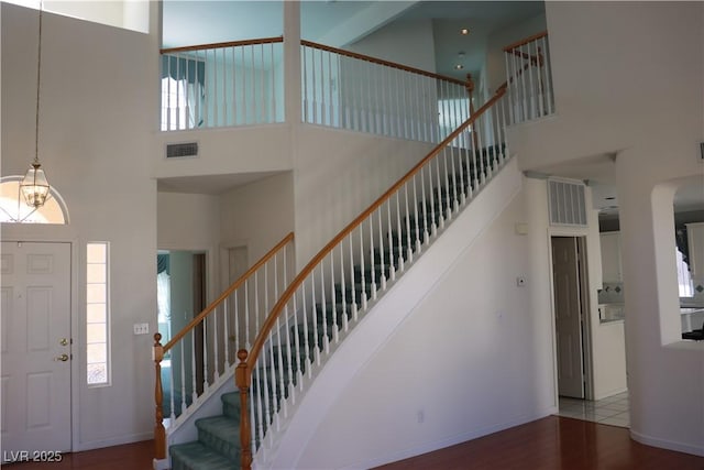 entryway featuring visible vents, wood finished floors, stairway, baseboards, and a towering ceiling