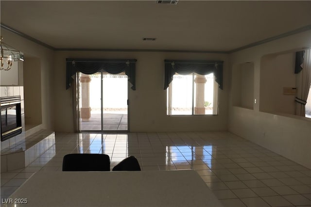 tiled empty room featuring visible vents, plenty of natural light, a notable chandelier, and ornamental molding