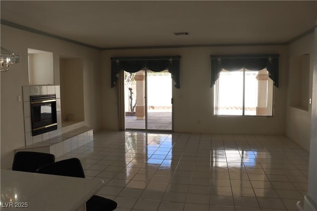 unfurnished room with visible vents, a notable chandelier, a tiled fireplace, crown molding, and light tile patterned floors