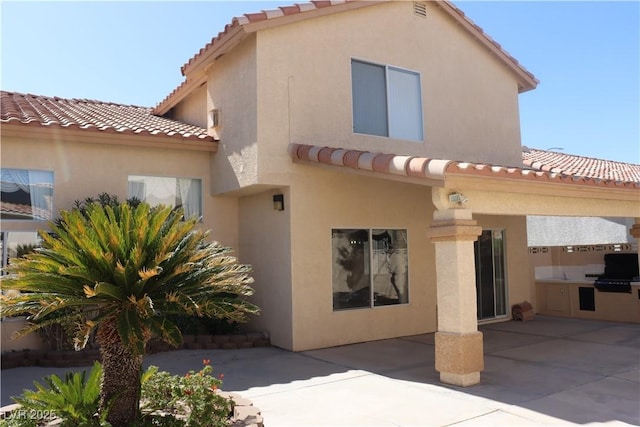 rear view of property with a patio area, area for grilling, stucco siding, and a tile roof