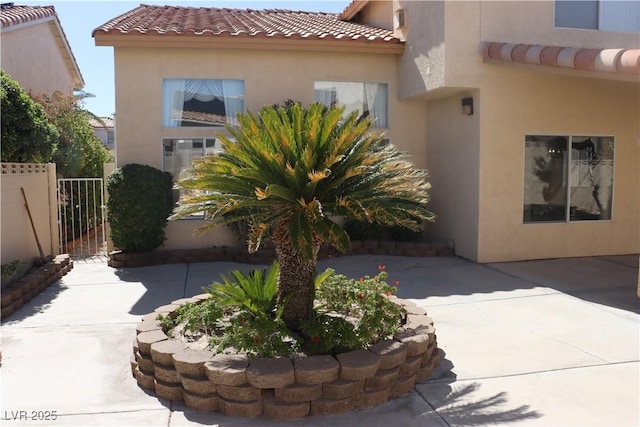 view of side of property with fence, a tiled roof, stucco siding, a patio area, and a gate