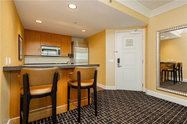 kitchen with dark countertops, recessed lighting, appliances with stainless steel finishes, and brown cabinetry