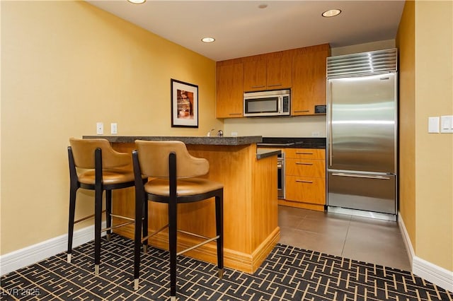 kitchen with dark countertops, brown cabinetry, a peninsula, and stainless steel appliances