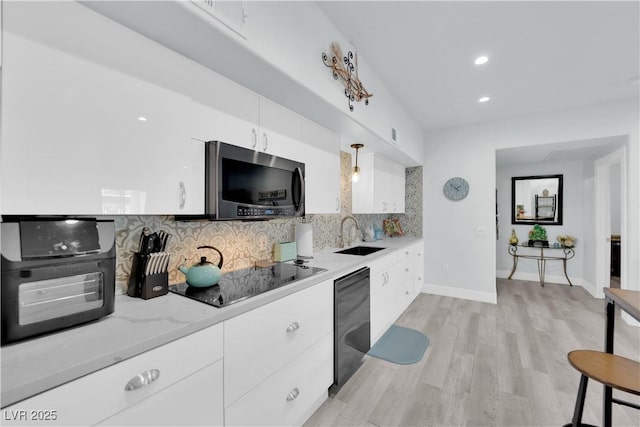 kitchen with light wood finished floors, a sink, decorative backsplash, black appliances, and white cabinetry