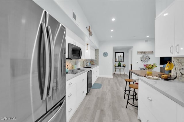 kitchen with backsplash, black appliances, light wood-style floors, white cabinetry, and a kitchen bar