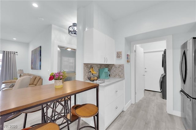 kitchen with tasteful backsplash, light countertops, stacked washer and clothes dryer, freestanding refrigerator, and white cabinetry