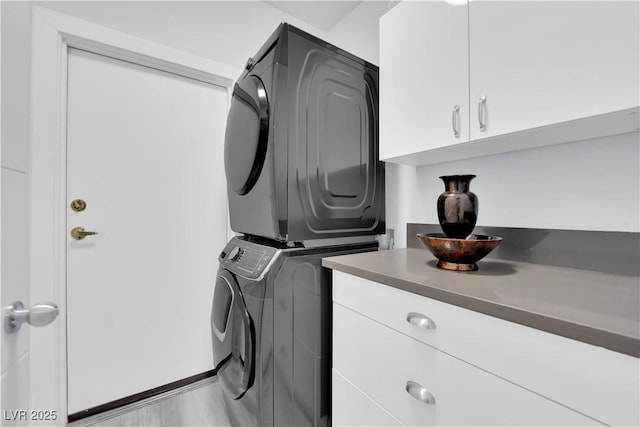 laundry area featuring light wood-style flooring, cabinet space, and stacked washer / drying machine