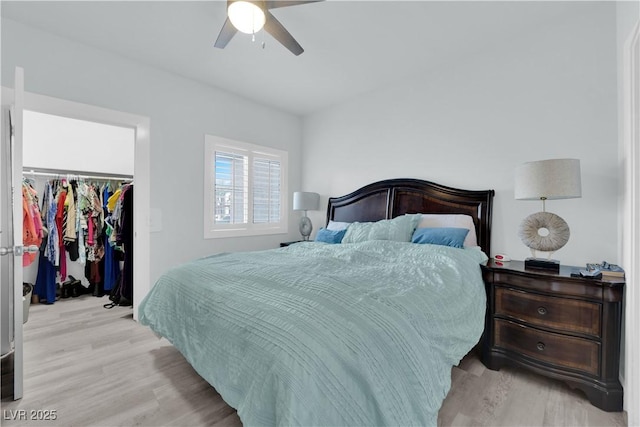 bedroom with a closet, light wood-style flooring, a walk in closet, and a ceiling fan