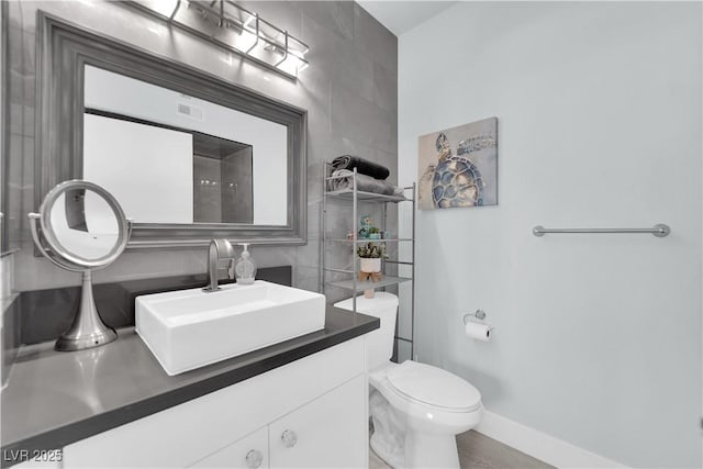 bathroom with vanity, tile walls, toilet, and baseboards