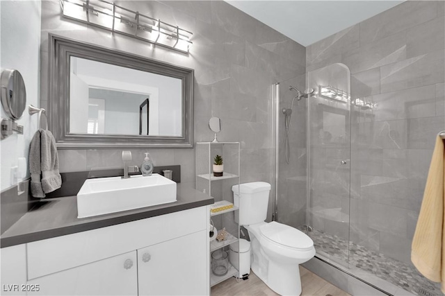 full bath featuring vanity, wood finished floors, a shower stall, tile walls, and toilet