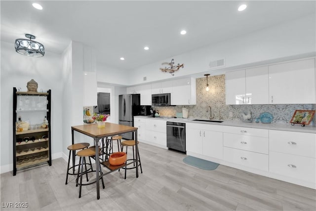 kitchen with visible vents, backsplash, white cabinets, stainless steel appliances, and a sink